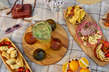 Assorted food and drinks arranged on a picnic blanket. Camera, sunglasses and other items are also...