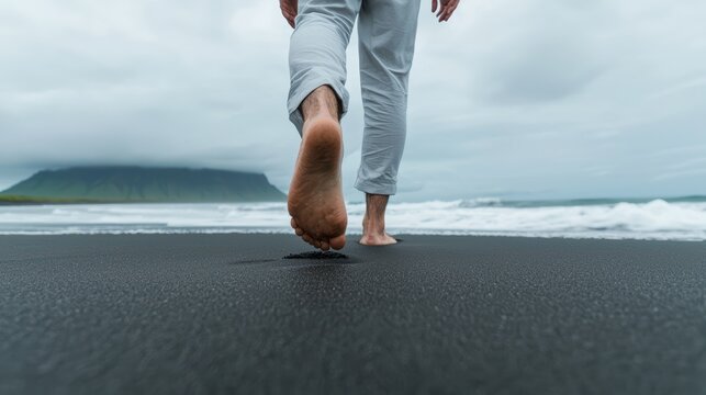 Walking barefoot on black sand beach, person expresses sense of tranquility and connection with nature. serene landscape enhances peaceful atmosphere. 