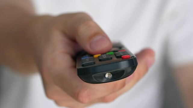 TV remote control.
A man watches TV.
A man's hand holds the TV remote control.
Buttons on the remote control.
TV, transmission, watch, buttons