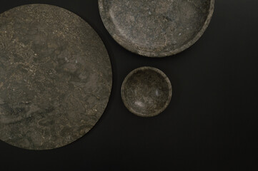 Top view of brown marble tray, plate and bowl on black background. Food presentation, dishes, stone tray. Copy space, flat lay.