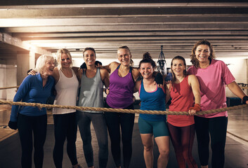 Smiling mature women standing together after a boxing gym workout. They stand up in the boxing ring and look directly into the camera. There are punching bags hanging from the ceiling behind them.
