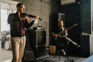 Musicians playing violin and bass guitar in recording studio. Focused performers practicing...