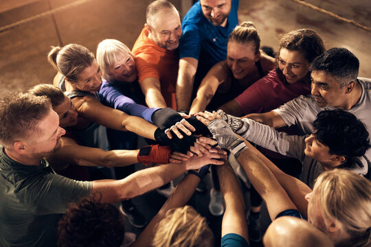 A large smiling diverse group standing with their hands in a huddle in a boxing gym. 