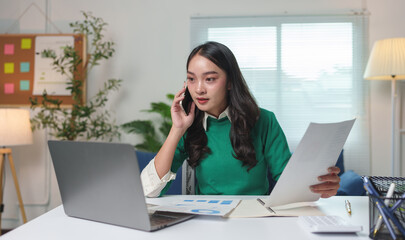 Young businesswoman talking on the phone at work Contacting customers in a modern office.To conduct business on a mobile phone at work using a laptop computer startup business idea.