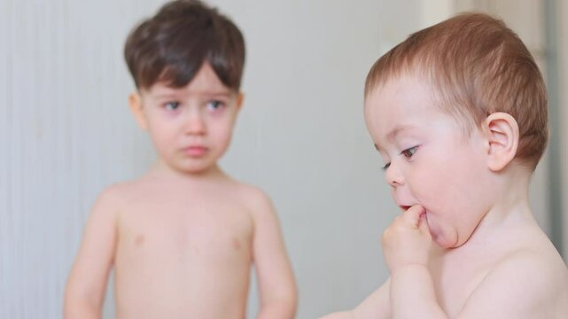 baby boy and kid in diaper walking in room,playing with wooden blocks,chewing some snack.portrait of siblings or friend.infant toddler stepping on weight scale.smiling child, close up,portrait.