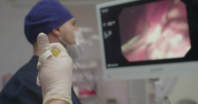 A doctor stares at a monitor during an endoscopy. An assistant holds endoscopic biopsy forceps in her hand. Taking a biopsy during an endoscopic examination.