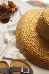 White blouse, straw hat, flat sansdals, tortoiseshell sunglasses, polka dot scrunchie, wicker bag and golden rings on white background. Summer outfit in neutral colors. Selective focus.