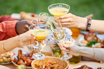 Gathering of friends raising glasses for a toast outdoors, sharing moments and enjoying food and drinks. Emphasis on camaraderie and festive setting