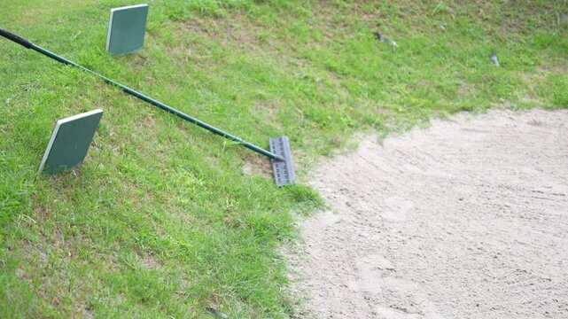 A green and black golf club is leaning against a green and brown grassy hill