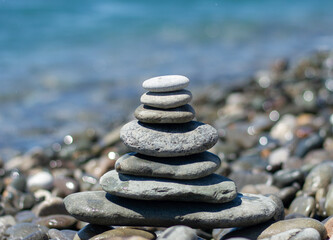 Balanced pebble pyramid silhouette on the beach with the sea