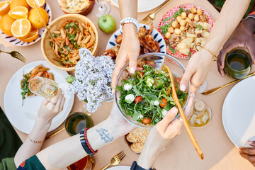 Table filled with variety of Mediterranean dishes being served, showing hands with plates and drinks capturing the vibrant communal meal setting, group gathering during daylight
