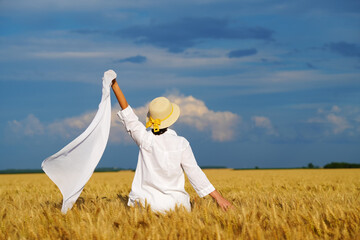 Young beautiful woman in a white dress on a Golden wheat field admiring the harvest.