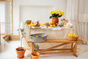 Vintage cozy interior of a room with a dining table and a wooden bench. Rustic Italian retro style. Kitchen utensils, candles, lemons, and a jug with yellow roses.