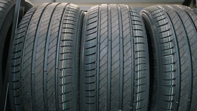 Close-up view of new winter tires on display at a car store. The tires are stacked on a shelf and have a variety of features, including aggressive tread patterns for traction in snow and ice