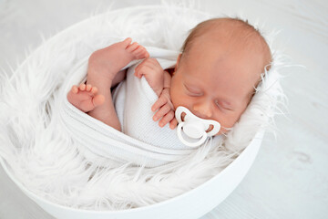 a newborn baby lies in a diaper on the bed and sucks a pacifier on a white isolated background, a place for text, a small baby boy is sleeping sweetly, a close-up portrait