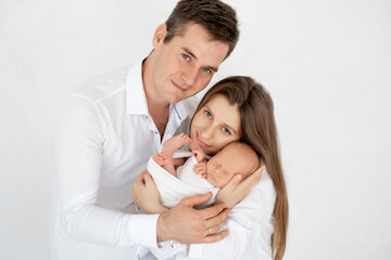 young parents with a newborn baby hug and kiss, happy mom and dad admiring the baby at home on the bed, a happy family caring for a small child, a place for text