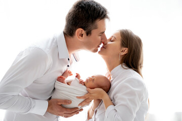 young parents with a newborn baby hug and kiss, happy mom and dad admiring the baby at home on the bed, a happy family caring for a small child, a place for text