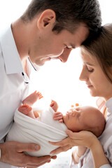 young parents with a newborn baby hug and kiss, happy mom and dad admiring the baby at home on the...