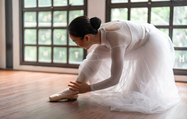 Ballerina in ballet shoes. Asian girl tying ribbons of toe shoes. ballet dancer preparing and wearing ballet shoes in dance studio prepares for a rehearsal.