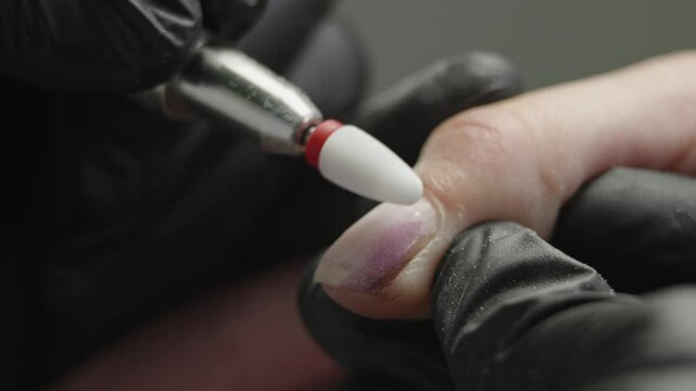 A woman manicure master makes a hardware manicure in black gloves removing the old coating of gel Polish in the salon. The concept of beauty professional nail care