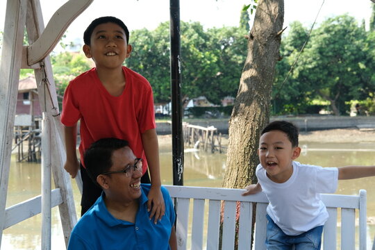 A father and his young son enjoying a calm moment together on a white outdoor swing by the river.
