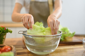 Close up shot of woman washing lettuce while preparing healthy vegan salad in kitchen