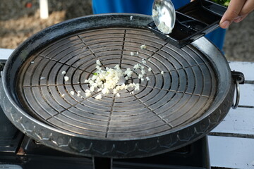 A close-up of garlic being added to a hot grill, perfect for BBQ recipes, cooking blogs, and...
