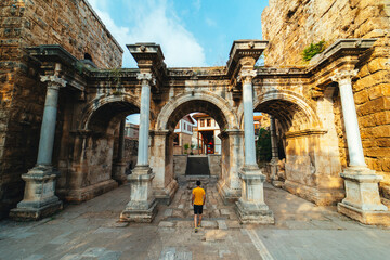 Obraz premium Hadrian's Gate. The three gates that are the symbol of Antalya. A man walks towards the gates. Wide angle photo taken on a cloudy day. Turkey.
