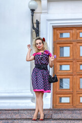 Blonde girl in a bright dress and sunglasses on the street near a building on a walk on a summer...