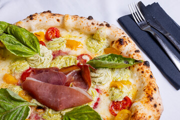 Pizza tradizionale napoletana con prosciutto crudo, pomodori rossi, pomodori gialli, ricotta e basilico fresco servita in una pizzeria elegante