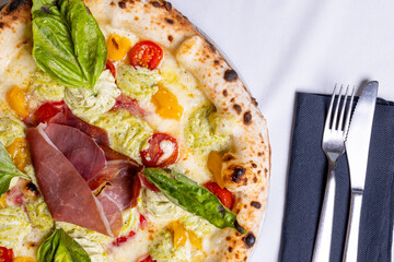 Pizza tradizionale napoletana con prosciutto crudo, pomodori rossi, pomodori gialli, ricotta e basilico fresco servita in una pizzeria elegante