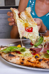 Pizza tradizionale napoletana con prosciutto crudo, pomodori rossi, pomodori gialli, ricotta e basilico fresco servita in una pizzeria elegante