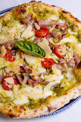 Pizza tradizionale napoletana con pesto di basilico, mozzarella, scaglie di formaggio, pomodori, pancetta croccante e basilico fresco servita in una pizzeria elegante