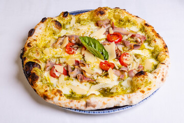 Pizza tradizionale napoletana con pesto di basilico, mozzarella, scaglie di formaggio, pomodori, pancetta croccante e basilico fresco servita in una pizzeria elegante