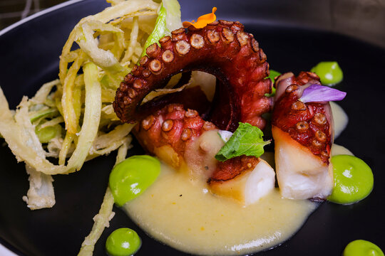 Polpo cotto alla brace e servito su una purea di patate e piselli con finocchi fritti come contorno in un ristorante di pesce elegante