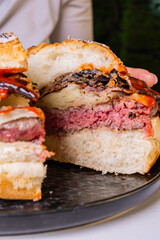 Panino da pub ripieno di hamburger di carne, melanzane grigliate, salsa bbq, bacon croccante e formaggio tagliato a metà e tenuto tra le mani da una cliente