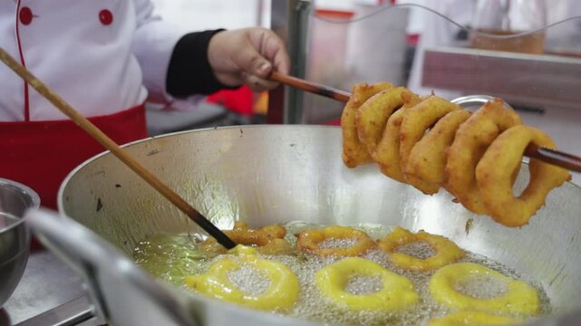 A woman is cooking picarones in a pan. Peruvian food