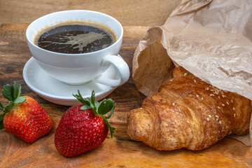 Fresh croissant and strawberries for tasty breakfast on wooden background.
