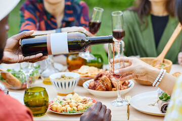 Group of friends sharing wine and enjoying a festive outdoor dinner gathering with assorted food on the table and lively conversation among participants