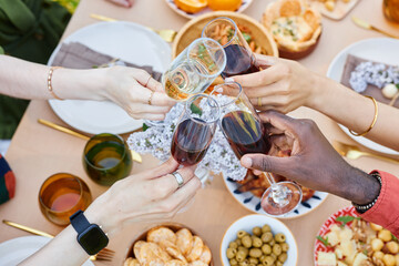 Hands of multi-ethnic group clinking wine glasses in festive gathering celebrating togetherness and diversity while enjoying delicious food and snacks on beautifully arranged table