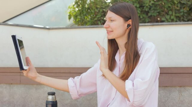 Young woman with headphones talking on video call on tablet in park. Close up. 