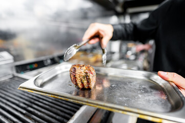 A close-up of a hand using tongs to flip a seasoned steak on a grill, with smoke rising, indicating cooking in progress. Ideal for culinary, food preparation, and gastronomy themes.