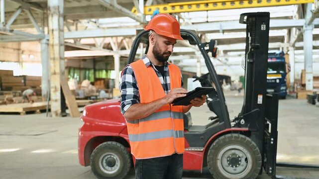 Caucasian Male Stocking Associate Doing Inventory On Tablet, Checking Delivery Tracking Number On Boxes. Man Working In Warehouse Facility With Conveyor Belt Packing Products For Online Customers.