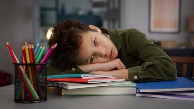 African American little son boy kid child sad upset frustrated fatigued exhausted lying on books at table at home homework problem education trouble stress tired learning studying insomnia lack energy