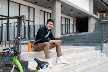 Young Professional Man Sitting Outdoors with Eco-Friendly Bicycle and Reusable Water Bottle in Modern Urban Setting