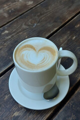 Freshly brewed white ceramic mug of hot, foamy cappuccino with decorative milk froth heart.