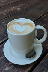 Freshly brewed white ceramic mug of hot, foamy cappuccino with decorative milk froth heart.