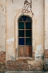 Window in old building ruin with crumbling cement walls revealing the brick structure.