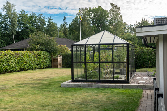 Beautiful greenhouse glass house based in foundation on the garden yard near the villa. There are lots of pots with various plants. Landscape garden design. Greenhouse for growing plants. 