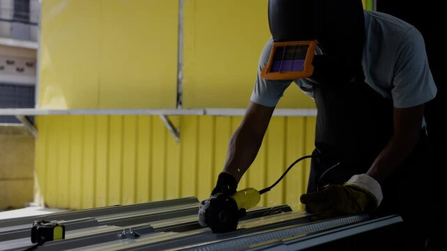 A worker hands cutting a metal sheet for roofing by using a grinder. Cutting a profile sheet with a grinder.